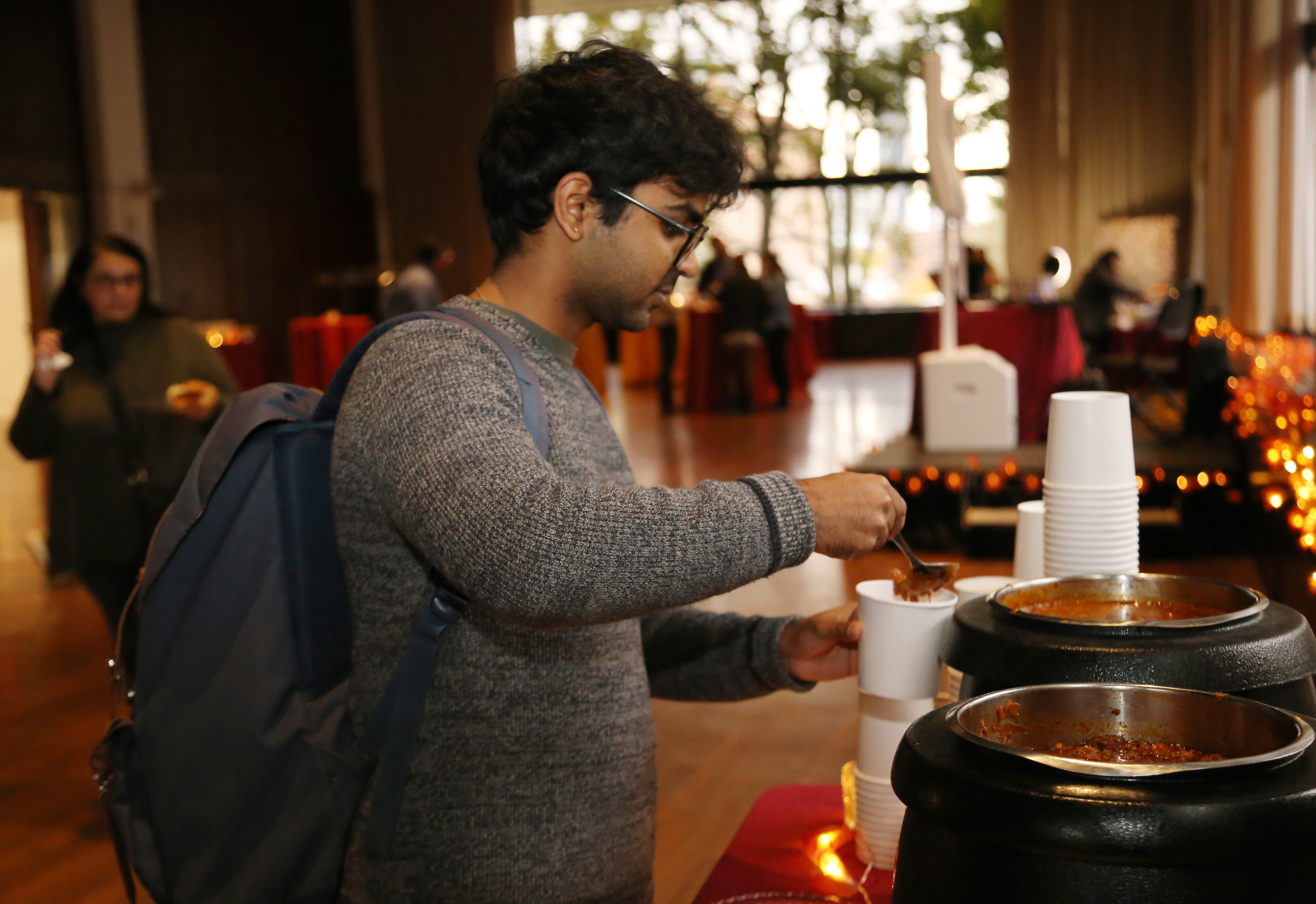 A fall fair attendee in a grey sweater and glasses samples food at a buffet table