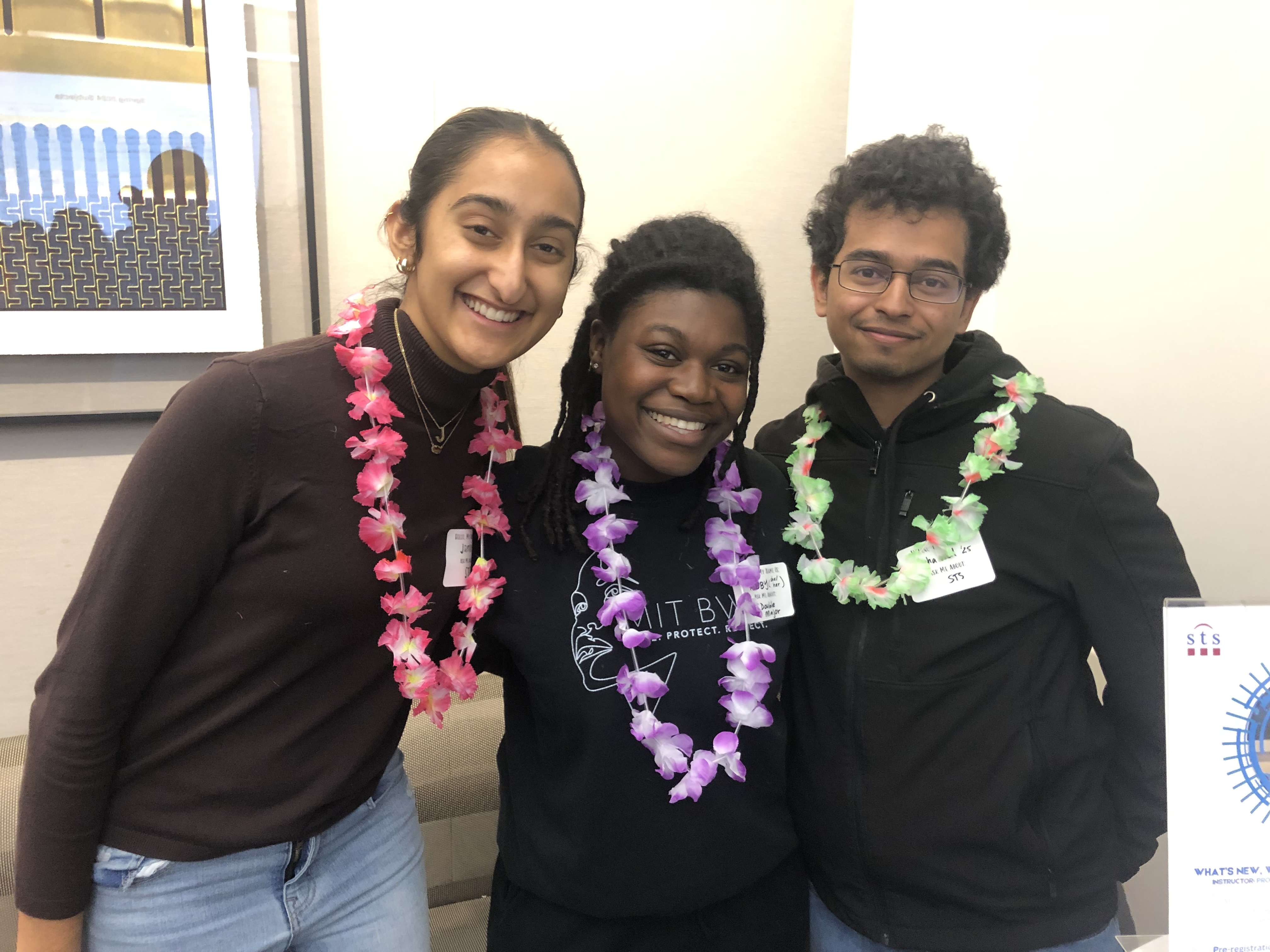 Three students in black shirts wear leis and smile during the Spring Ahead with SHASS event