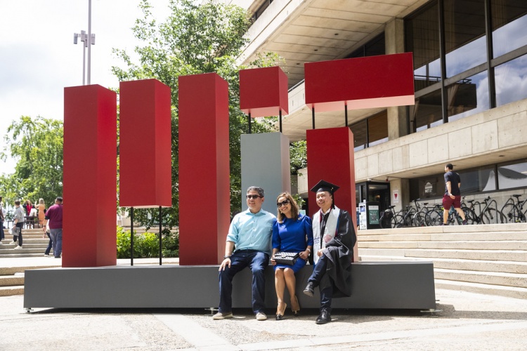 MIT parents and student post-graduation sitting in front of large MIT sign 