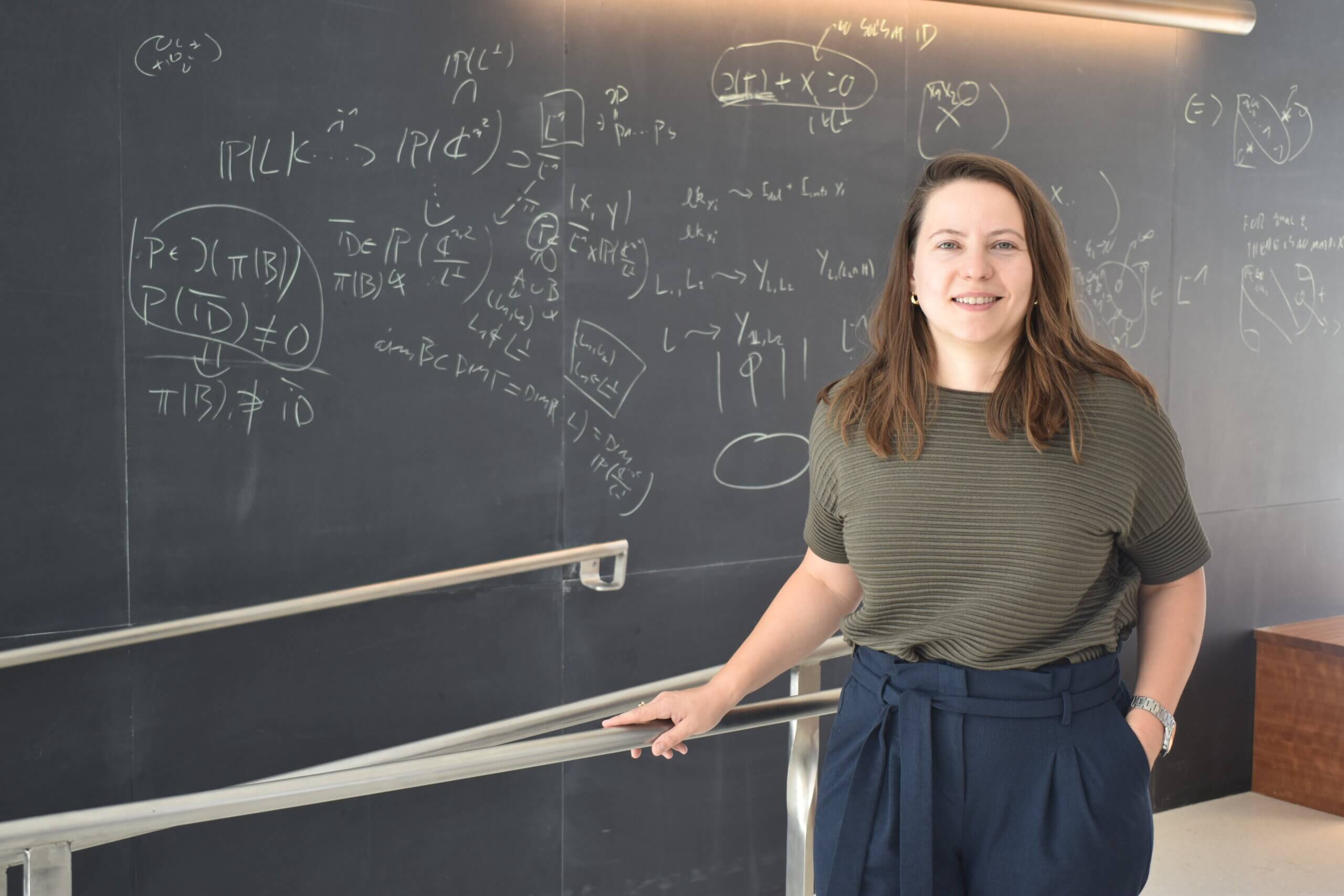 MIT alumna Alex Reiss Sorokin stands near a blackboard